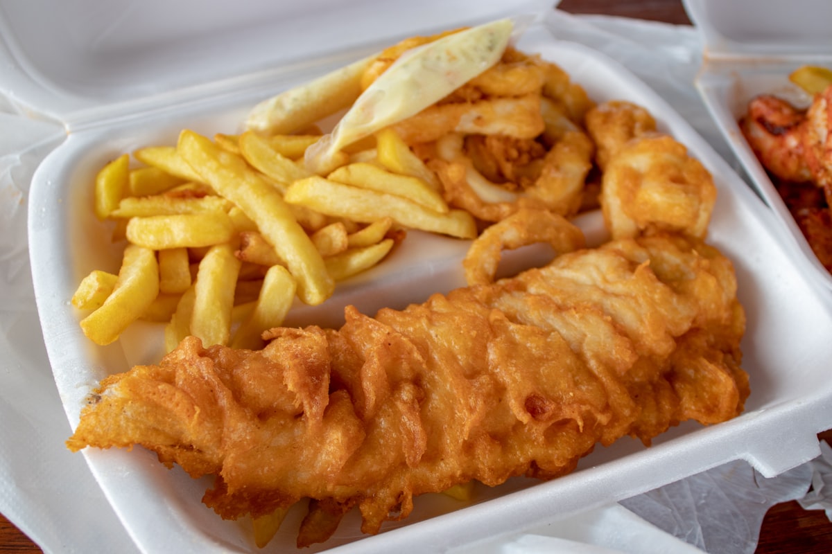 Battered fish and thick cut chips in an open takeaway tray with a lemon wedge