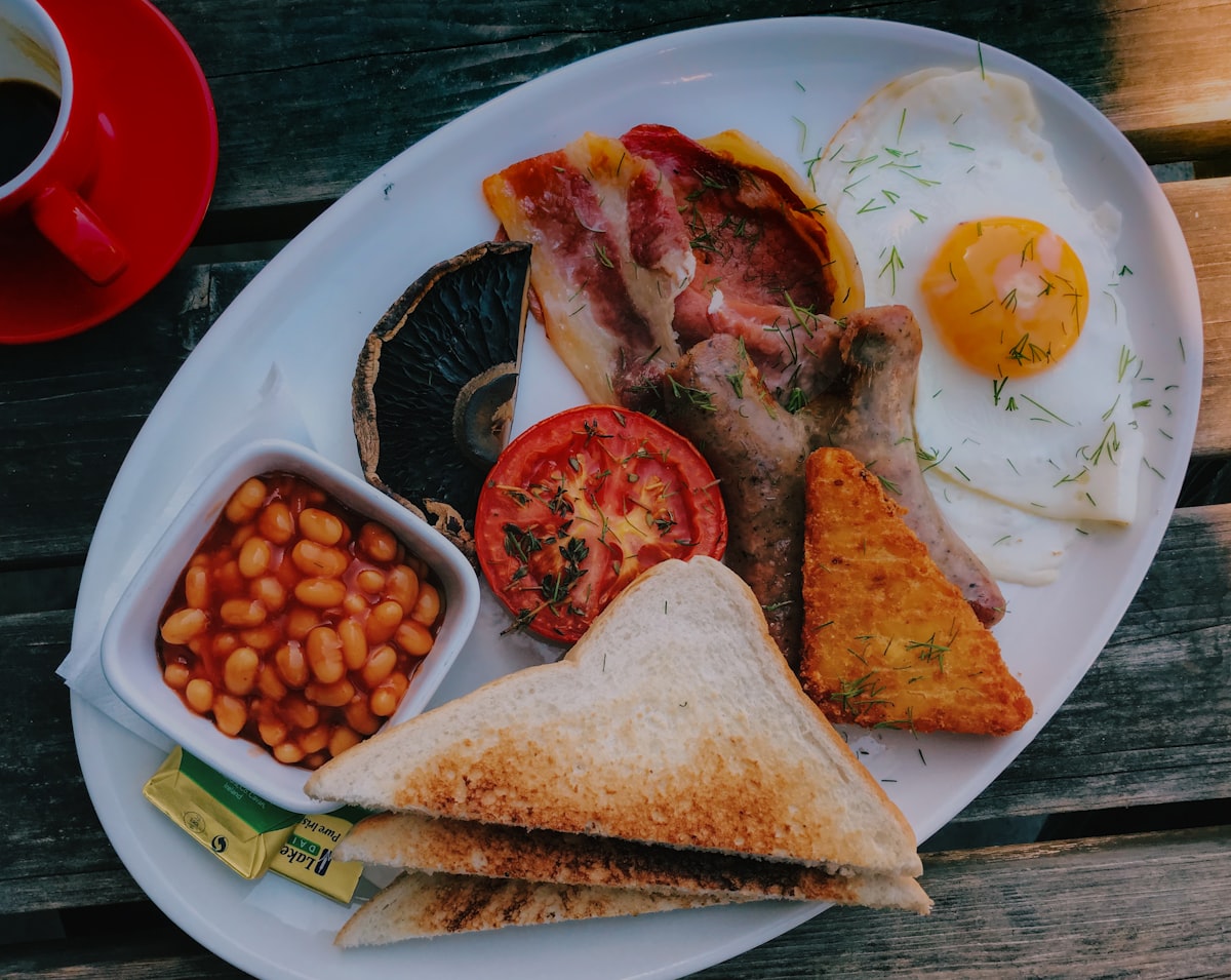 A full English breakfast with bacon, fried eggs, beans, tomato, sausage and toast on a plate