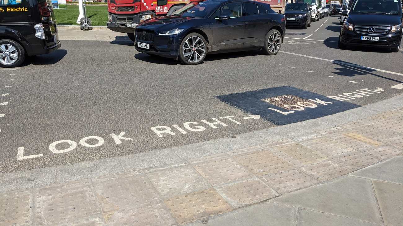 The words LOOK RIGHT painted twice in white on the road at a London crossing with black cars waiting beyond