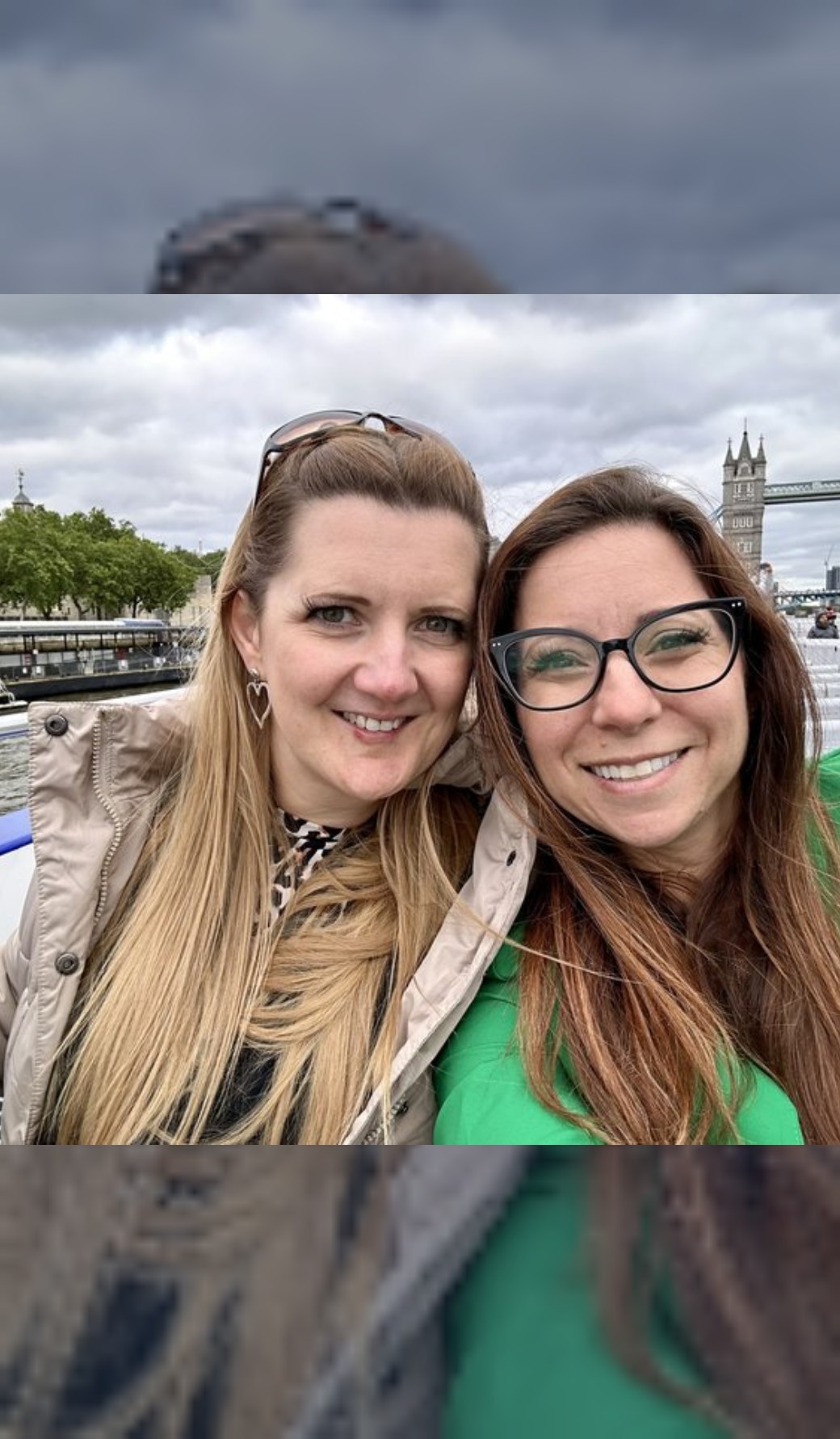 Nicole and a friend with their heads together, smiling, on a grey London day by the Thames