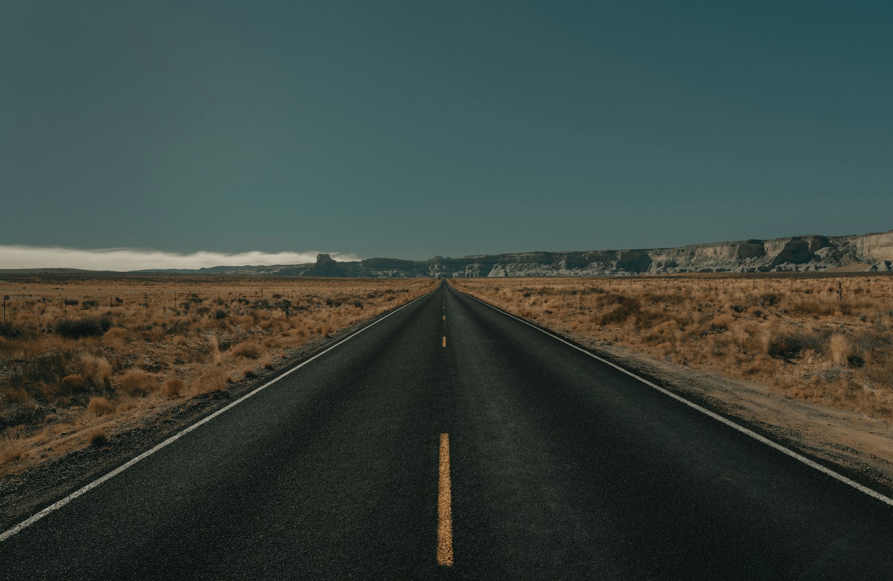 A black asphalt road running straight between brown grass fields in Utah