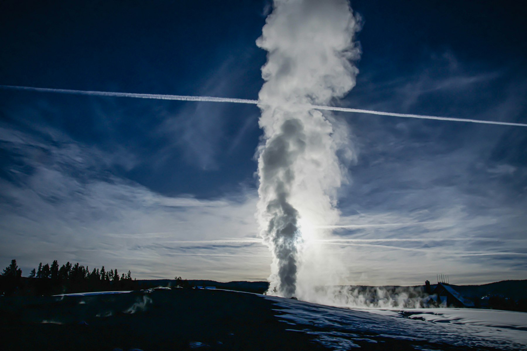 Old Faithful sending a tall column of water and steam into a dark blue sky