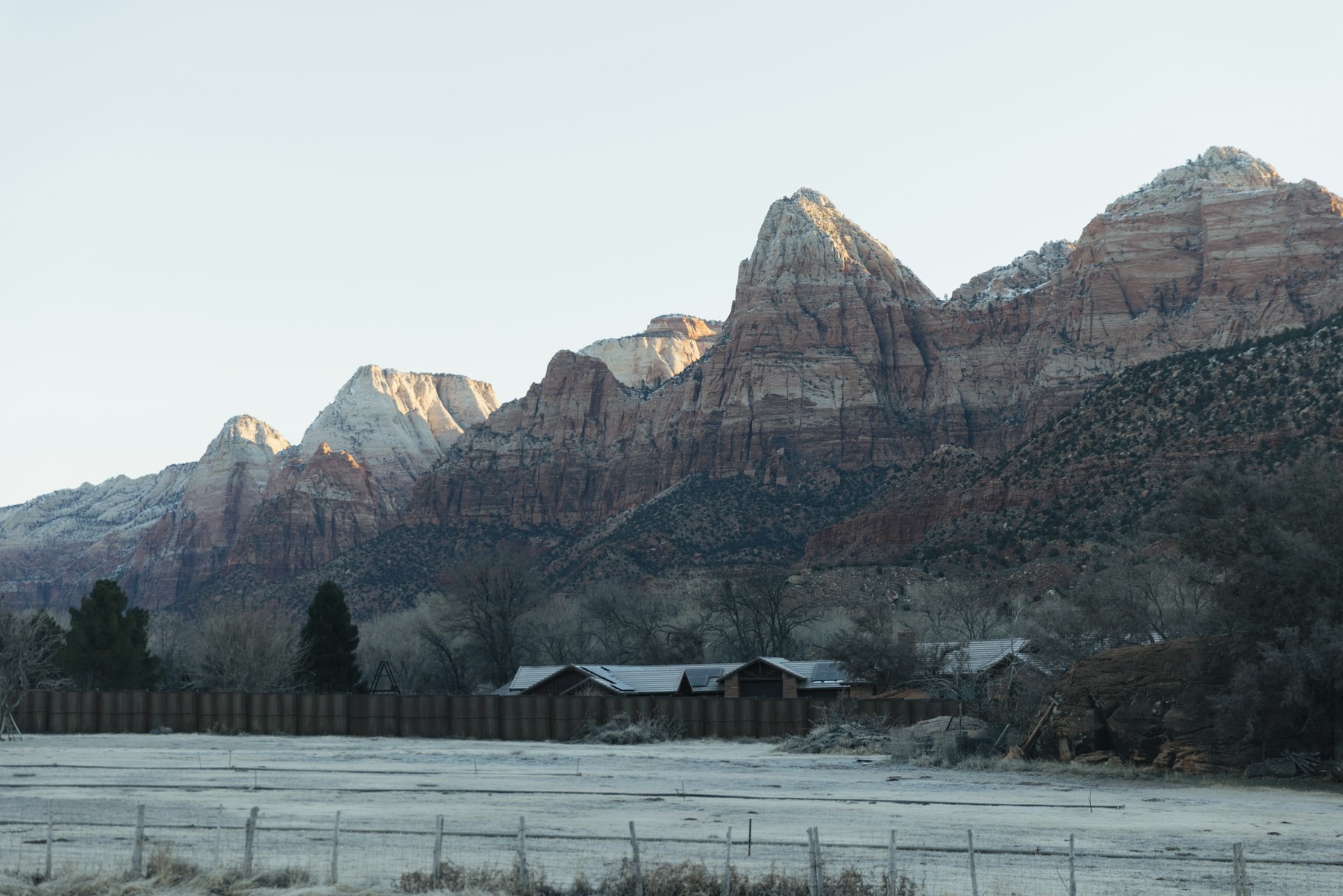 Low wooden buildings on the valley floor below the snow dusted peaks of Zion National Park