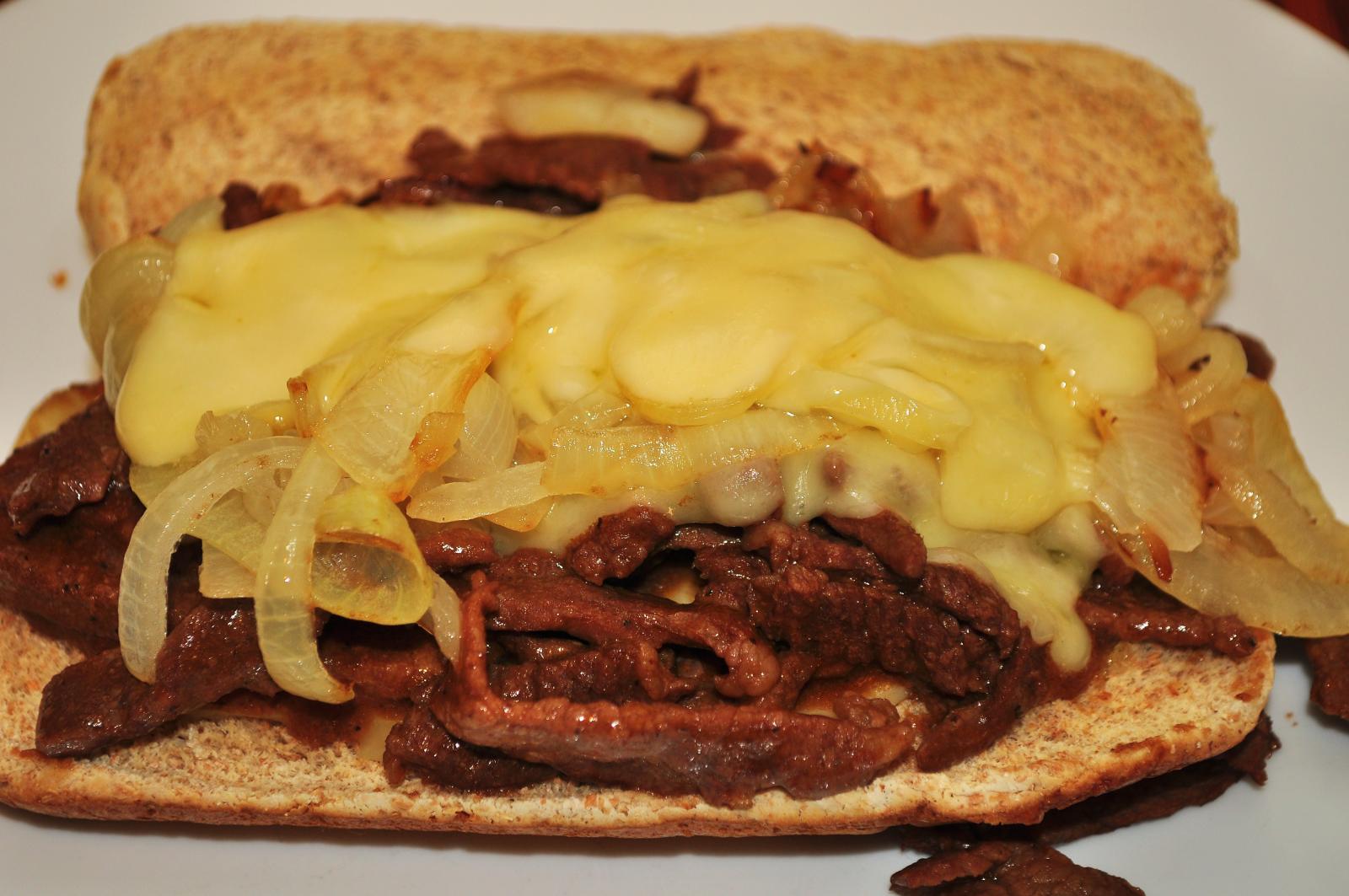 A Philly cheesesteak sandwich with melted cheese and grilled onions on a soft roll